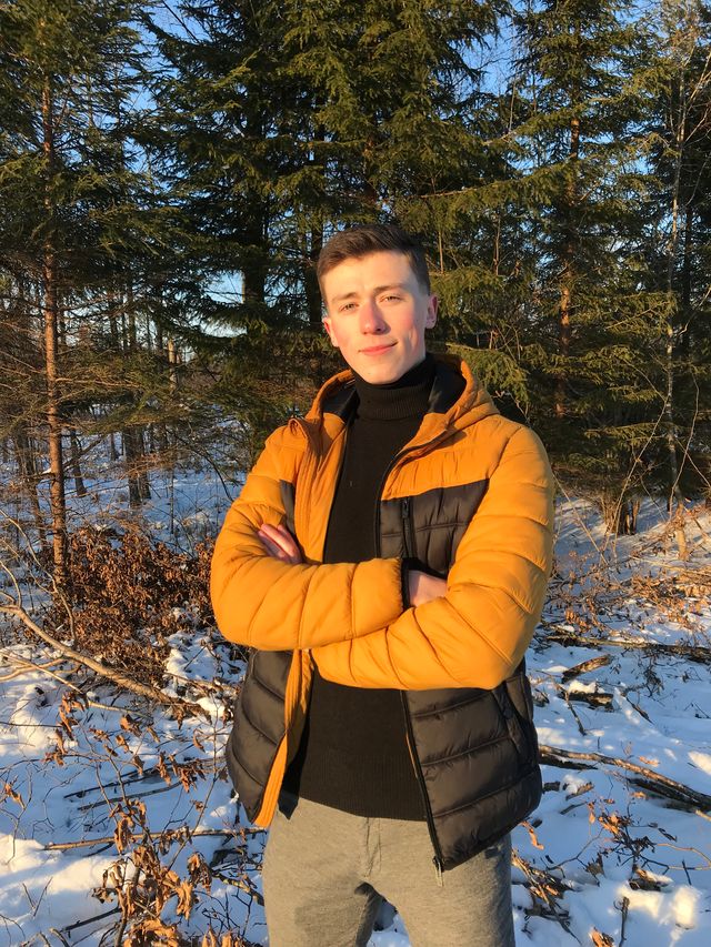 Photo of Bogumił Milewski, standing in a yellow and black jacket in the background of trees in winter